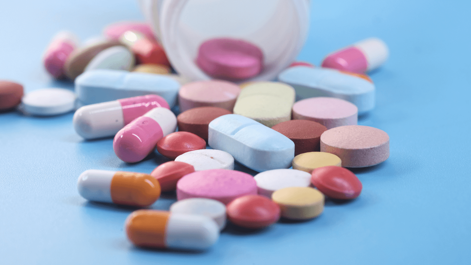 Comprimidos e pílulas espalhados numa superfície azul